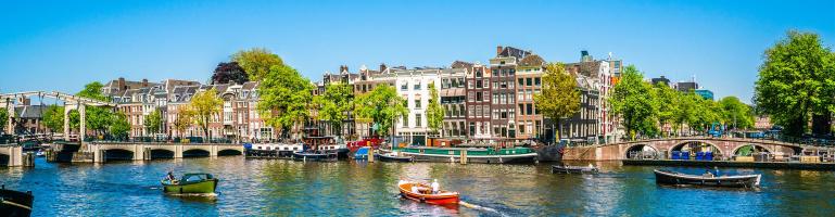Panoramafoto der Grachten von Amsterdam, Niederlande, mit Grachtenhäusern und Brücke mit vorbeifahrenden Schaluppen | Seacon Logistics